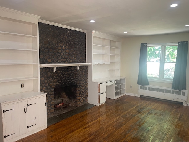 unfurnished living room with dark wood-type flooring, a large fireplace, built in shelves, and radiator heating unit