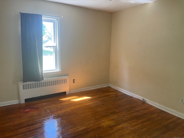 empty room with dark hardwood / wood-style flooring and radiator heating unit