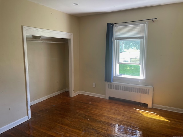 unfurnished bedroom featuring dark hardwood / wood-style flooring, radiator, and a closet