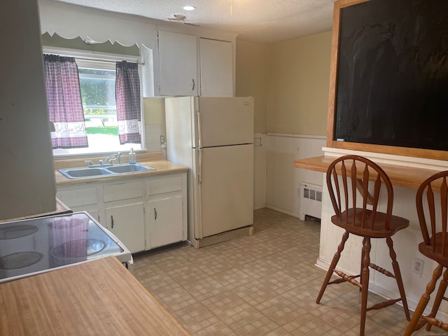 kitchen with sink, white cabinetry, white fridge, and radiator