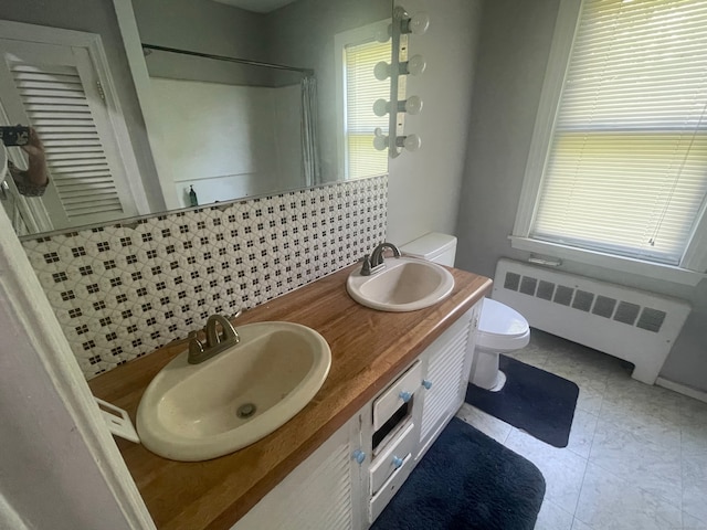 bathroom with double sink vanity, tile flooring, radiator, and toilet