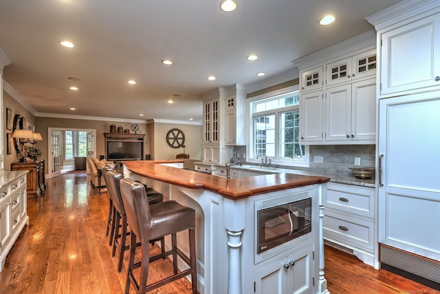 kitchen with stainless steel microwave, wood-type flooring, backsplash, crown molding, and white cabinetry