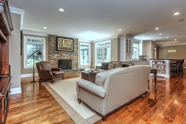 living room featuring a stone fireplace, ornamental molding, an inviting chandelier, and hardwood / wood-style floors