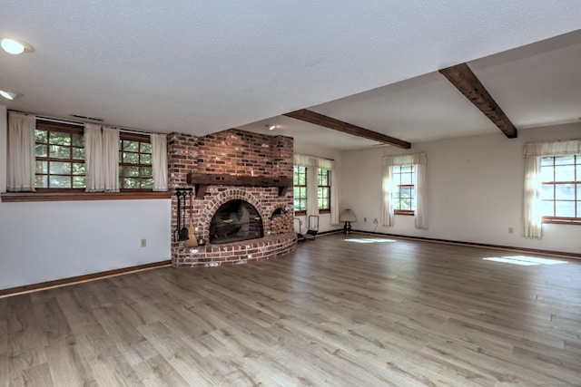 unfurnished living room featuring beamed ceiling, light wood-type flooring, a brick fireplace, and a healthy amount of sunlight