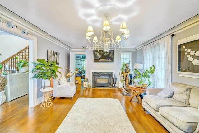 living room with a high end fireplace, wood-type flooring, crown molding, and a notable chandelier