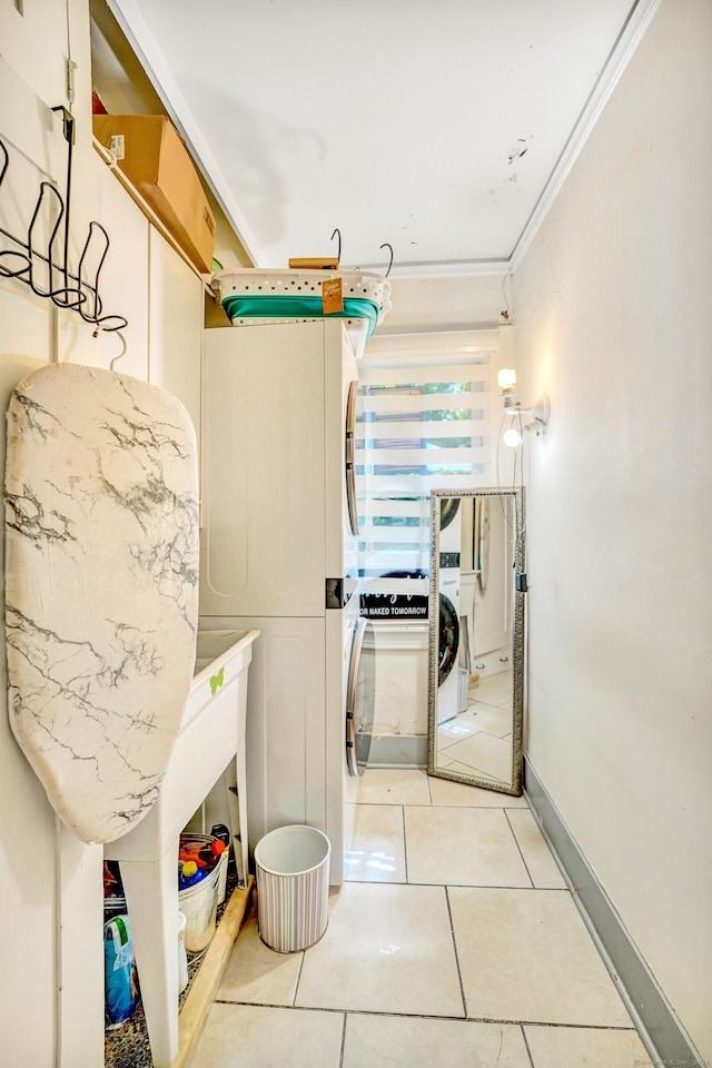 clothes washing area featuring tile patterned flooring, crown molding, and stacked washer and dryer