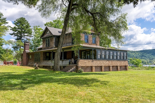 rear view of property featuring a sunroom, a mountain view, and a yard