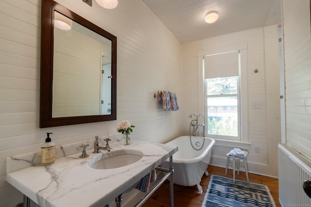 bathroom featuring wood walls, radiator heating unit, a bathtub, and hardwood / wood-style floors