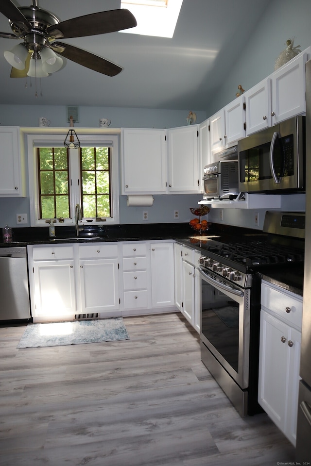 kitchen with stainless steel appliances, sink, vaulted ceiling with skylight, light hardwood / wood-style floors, and ceiling fan