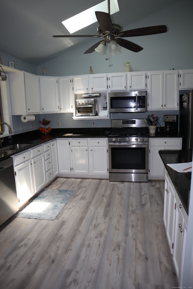 kitchen with white cabinets, appliances with stainless steel finishes, light wood-type flooring, and vaulted ceiling with skylight