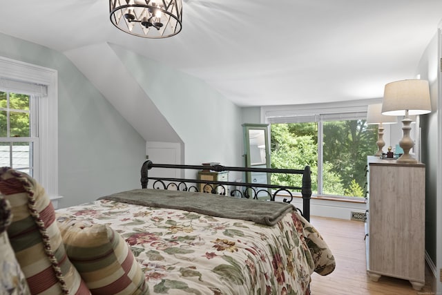 bedroom featuring an inviting chandelier, lofted ceiling, and light hardwood / wood-style floors