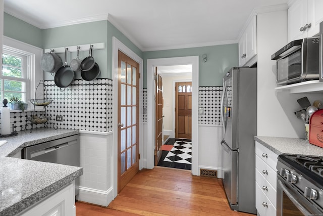 kitchen with light hardwood / wood-style flooring, ornamental molding, white cabinets, and appliances with stainless steel finishes