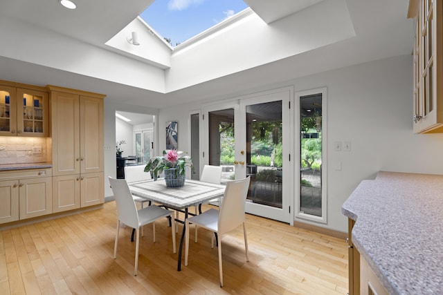 dining space with light hardwood / wood-style flooring, french doors, and vaulted ceiling with skylight