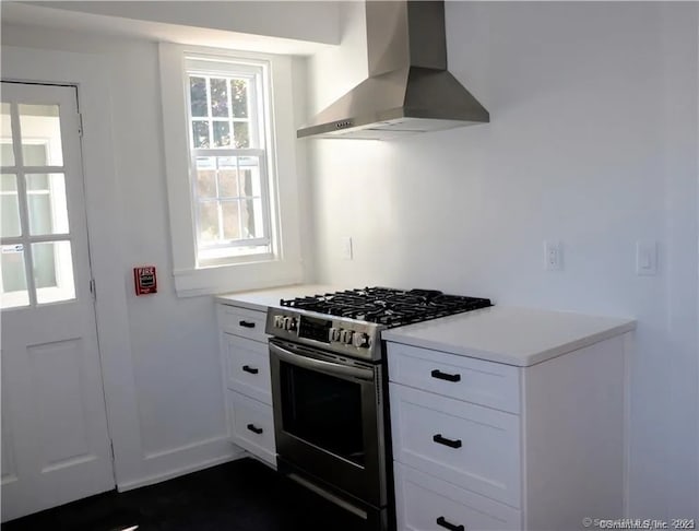 kitchen with high end stove, white cabinets, plenty of natural light, and wall chimney exhaust hood