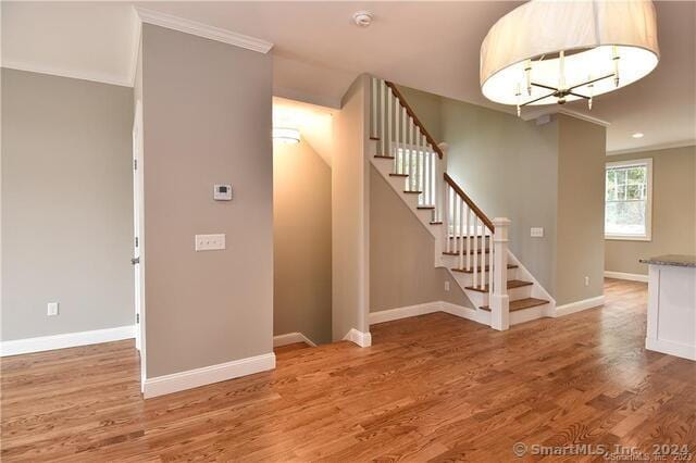 staircase with an inviting chandelier, crown molding, baseboards, and wood finished floors