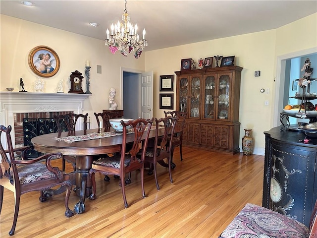 dining room featuring light hardwood / wood-style flooring, a fireplace, and an inviting chandelier