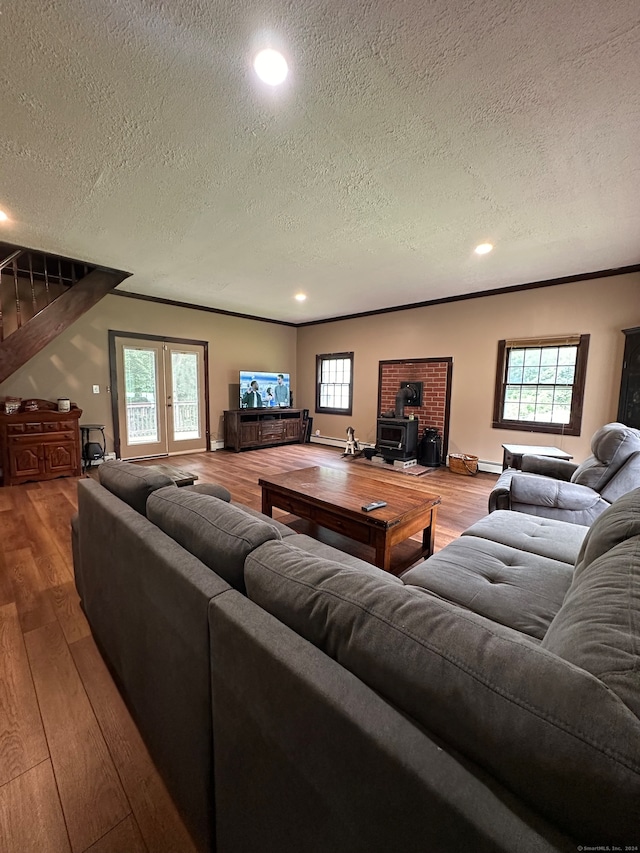 living room featuring a wood stove, a textured ceiling, light hardwood / wood-style flooring, a baseboard heating unit, and crown molding