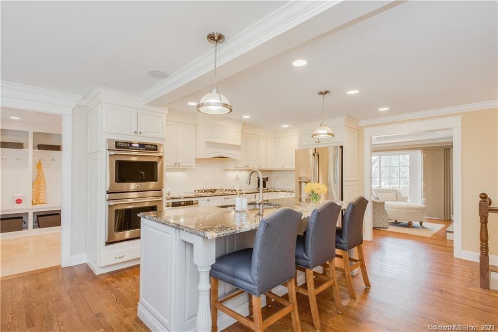 kitchen featuring light stone countertops, appliances with stainless steel finishes, decorative light fixtures, a center island with sink, and white cabinetry