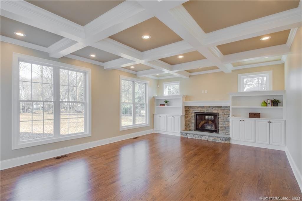 unfurnished living room with beamed ceiling, plenty of natural light, wood-type flooring, and a fireplace