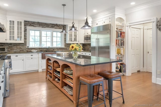 kitchen with built in appliances, white cabinetry, a center island, and light wood-type flooring