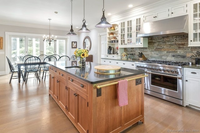 kitchen with pendant lighting, white cabinets, range with two ovens, ornamental molding, and a center island with sink