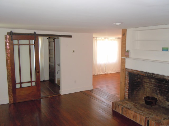 unfurnished living room with a brick fireplace, hardwood / wood-style floors, and a barn door