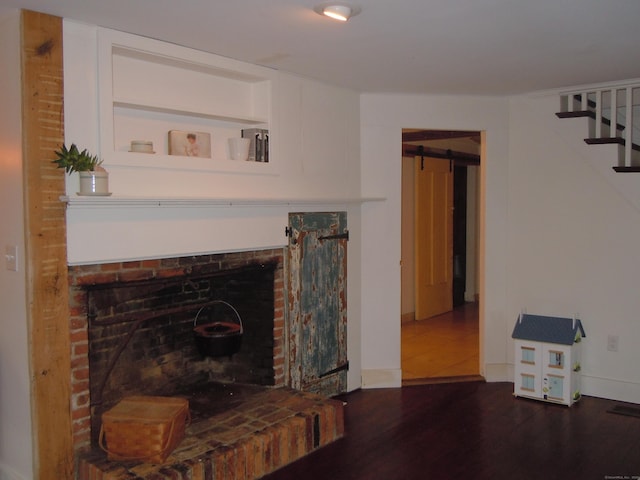 living room with a fireplace, built in features, dark hardwood / wood-style floors, and a barn door