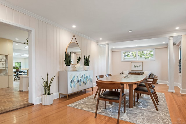 dining space with decorative columns, crown molding, and light wood-type flooring