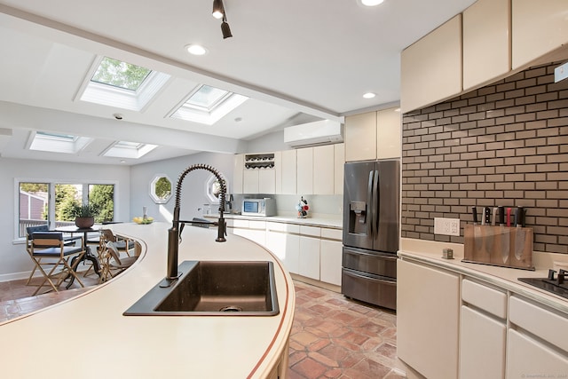 kitchen featuring stainless steel refrigerator with ice dispenser, lofted ceiling with skylight, a wall unit AC, sink, and light tile patterned floors