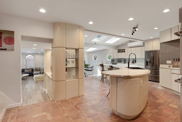 kitchen featuring a wall mounted air conditioner, lofted ceiling with skylight, a breakfast bar area, appliances with stainless steel finishes, and backsplash