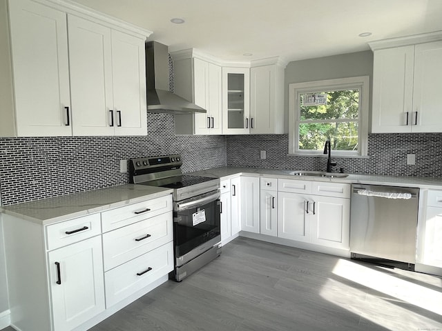 kitchen with white cabinetry, sink, stainless steel appliances, wall chimney range hood, and light wood-type flooring