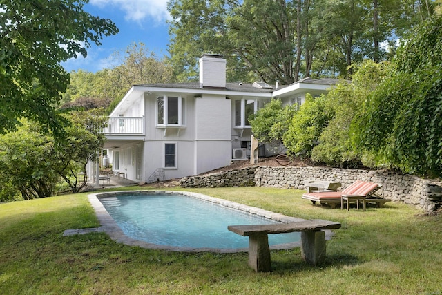 rear view of house with cooling unit, a yard, and a balcony