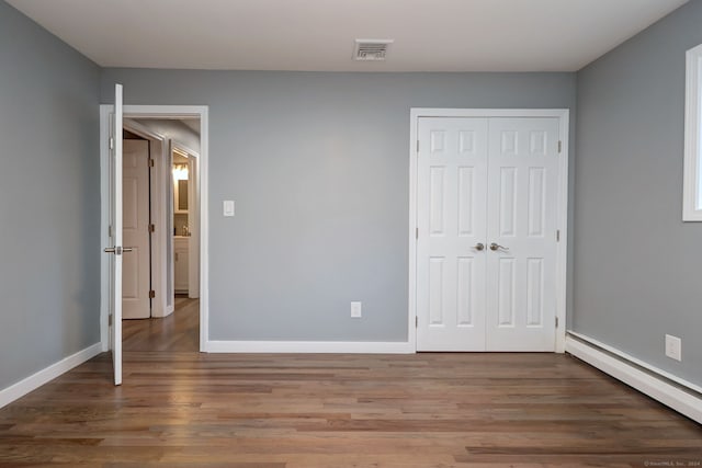 unfurnished bedroom with hardwood / wood-style flooring, a baseboard radiator, and a closet