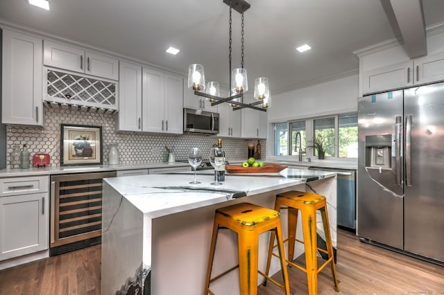 kitchen featuring wine cooler, appliances with stainless steel finishes, an island with sink, a kitchen breakfast bar, and light stone counters