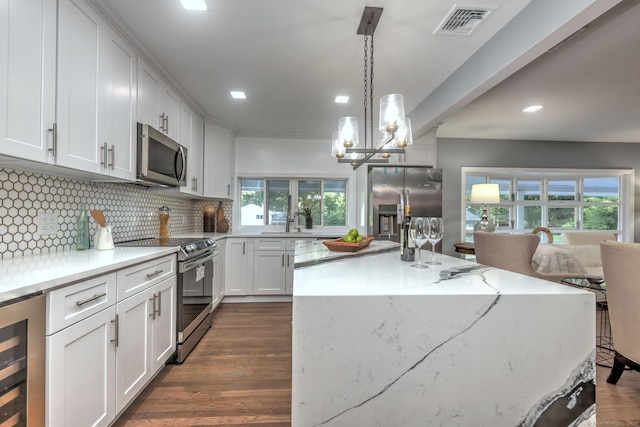 kitchen with appliances with stainless steel finishes, beverage cooler, decorative light fixtures, white cabinetry, and a center island with sink