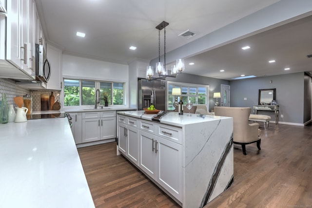 kitchen with a center island with sink, stainless steel appliances, dark wood-type flooring, hanging light fixtures, and white cabinets