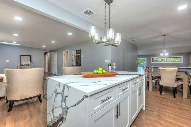 kitchen with hanging light fixtures, light stone countertops, white cabinetry, and a kitchen island