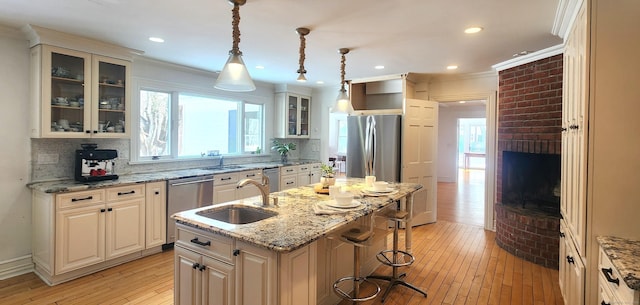 kitchen featuring a breakfast bar area, a center island with sink, light wood-style floors, appliances with stainless steel finishes, and crown molding