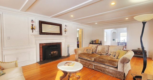 living area with beam ceiling, light wood-style flooring, crown molding, and a decorative wall