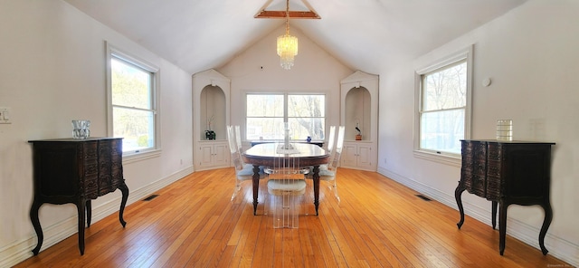 dining room with light wood finished floors, visible vents, arched walkways, and lofted ceiling