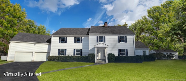 colonial home featuring aphalt driveway, roof with shingles, a front yard, a garage, and a chimney