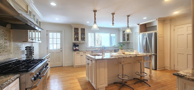 kitchen featuring light wood-type flooring, a center island with sink, under cabinet range hood, a sink, and stainless steel appliances