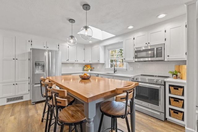 kitchen featuring sink, light hardwood / wood-style flooring, white cabinetry, stainless steel appliances, and decorative light fixtures