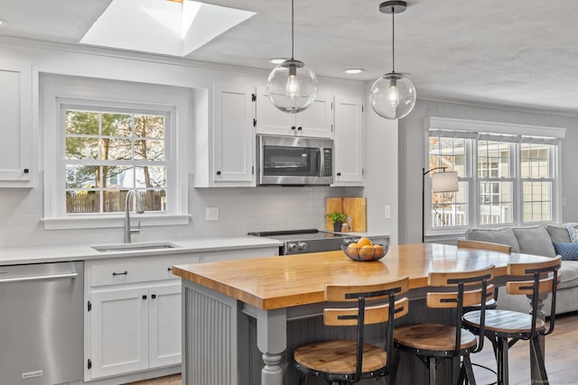 kitchen with appliances with stainless steel finishes, a breakfast bar, tasteful backsplash, white cabinetry, and sink