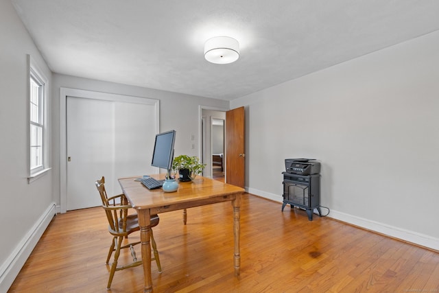 home office featuring light hardwood / wood-style flooring, a wood stove, and baseboard heating