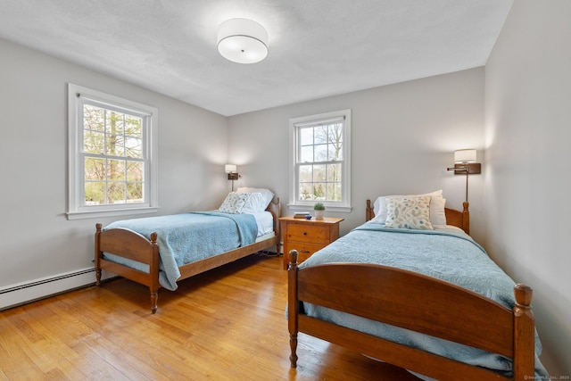 bedroom with multiple windows, a baseboard heating unit, and light hardwood / wood-style floors