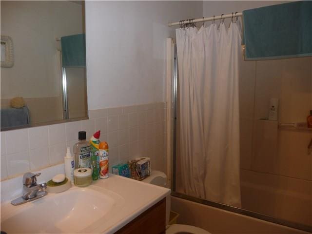 full bathroom featuring tile walls, shower / bath combo, decorative backsplash, toilet, and vanity