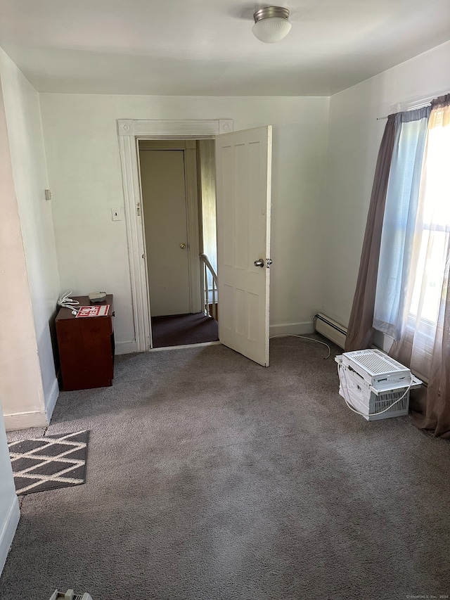 unfurnished room with baseboard heating, dark carpet, and a wealth of natural light