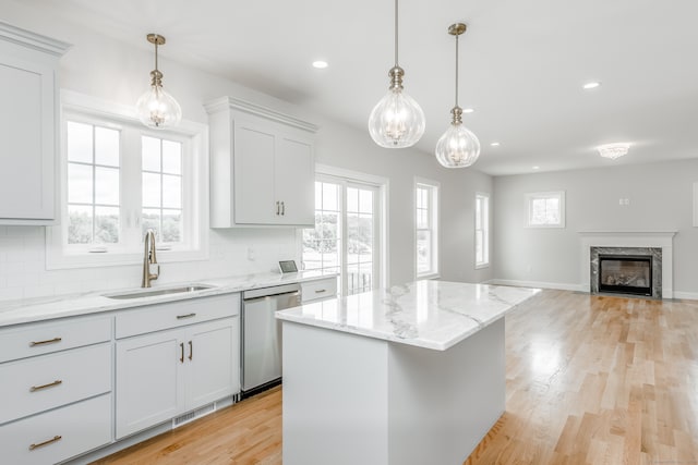 kitchen with a premium fireplace, tasteful backsplash, light hardwood / wood-style floors, stainless steel dishwasher, and a center island