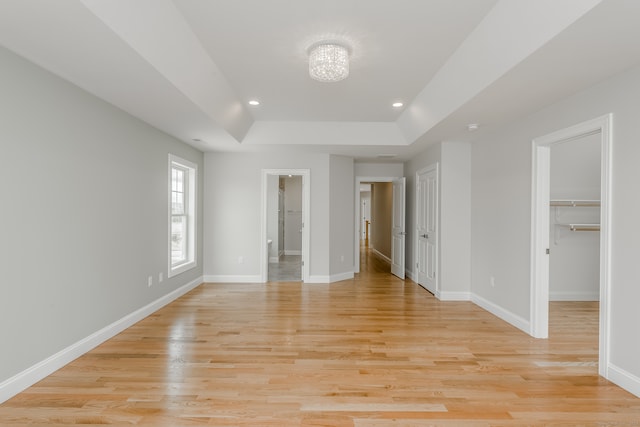 unfurnished bedroom featuring light hardwood / wood-style floors, a walk in closet, and a tray ceiling